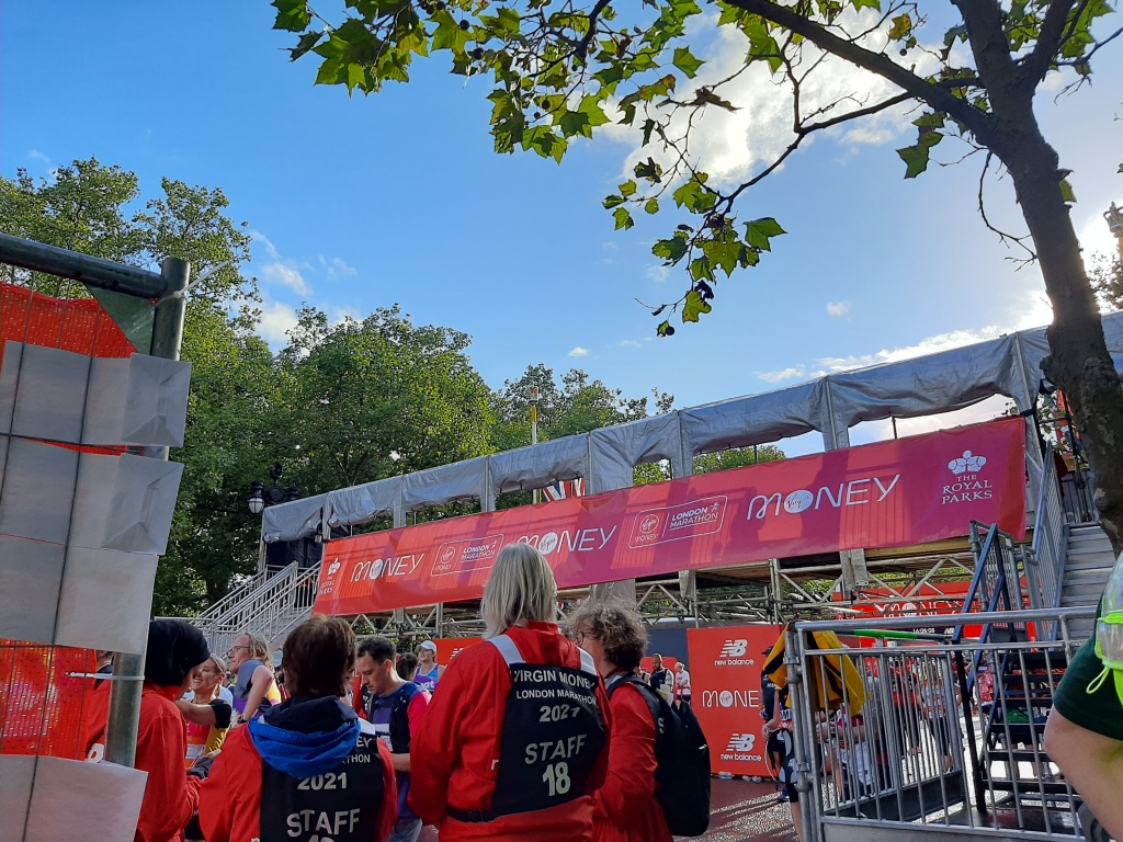 A massive arch with a banner with marathon logos on. In the foreground, several staff members in red windbreakers and tabards with their backs facing the camera